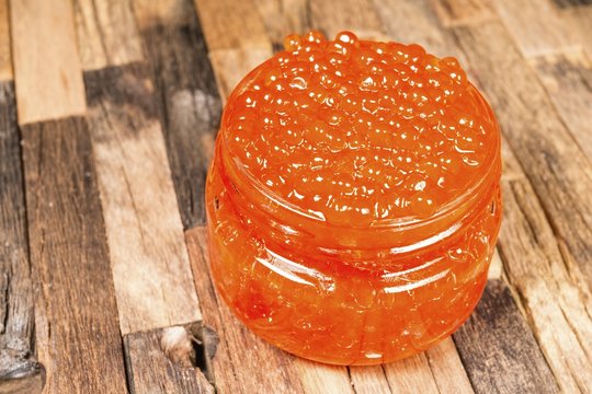 Caviar in glass jar on wooden background. Macro shot.