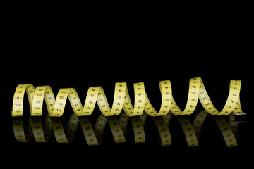 Fototapeta premium Yellow tape measure background - coiled on black, long.