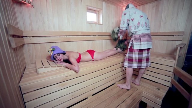 Young sexy girl sweating in the in wooden sauna. Lady hover brooms. HD.
