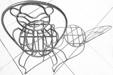 Black and white picture of wrought iron chair in intense light with shadow