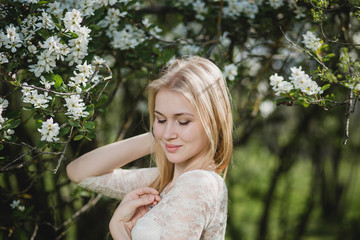 Naklejka premium Young beautiful blonde woman in blooming garden. Delicate girl enjoys spring nature
