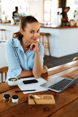 Learning, Studying. Portrait Of Beautiful Happy Smiling Student Woman Using Laptop Computer, Notebook, Writing, Taking Notes At Cafe. Female Freelancer Working. Freelance Work, Business People Concept