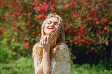 Happy lovely blond female sitting in blooming garden, woman with closed eyes enjoying  beauty of nature, relaxation at countryside