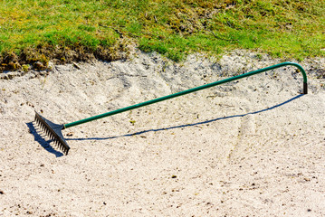 Rake lying in a sand bunker at a golf course one sunny day.