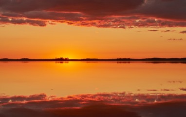 Fototapeta na wymiar Orange and red sky after the sunset at a lake in Finland. Symmetrical reflection of clouds in the still water.