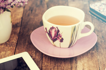 still life with tea cup and the contents of a work space composed. Different objects on wooden table. tablet,phone with headphones and spring flowers