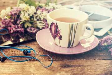 still life with tea cup and the contents of a work space composed. Different objects on wooden table. tablet,phone with headphones and spring flowers