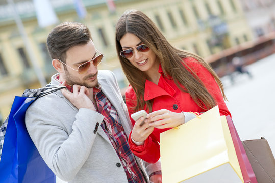 Young happy couple with smart phone and shopping bags