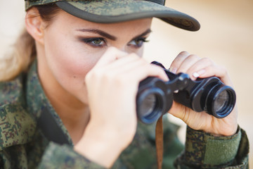 Gorgeous young woman in a Military costume with a binoculars on the background of a dessert