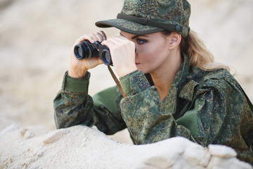 Gorgeous young woman in a Military costume with a binoculars on the background of a dessert