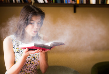 Portrait of young woman blowing off the dust from the book in library