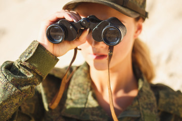 Gorgeous young woman in a Military costume with a binoculars on the background of a dessert