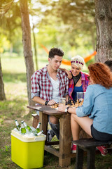 Boys and girls in pair play chess and drinks cold beer in nature