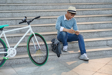 Stylish Vietnamese man sitting on the steps and text messaging