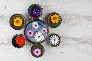 Colorful flowers floating in water in ceramic bowls on rustic wooden table. Top view with copy space.
