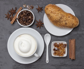 Coffe, a cup of hot latte or cappuccino with bun, top view. Background plate made from natural slate. Coffe beans, sugar, cinnamon and decorative star anise for love drink. Coffee shop