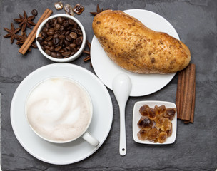 Cup of coffee with milk foam and biscuits and coffee beans lying on a black stone stand, top view. Delicious breakfast with a nice cup of coffee and desert for morning day. Original food.
