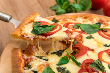 Pizza Margherita with tomatoes, mozzarella and basil on a wooden background, a slice of pizza with cheese stretching, close-up