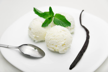Three scoops of ice cream with mint and a vanilla bean on a white plate, white background, close-up