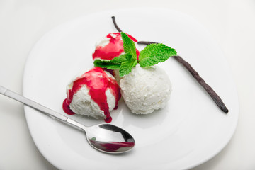 Three scoops of vanilla ice cream with strawberry syrup and mint on a white plate and a vanilla bean, white background