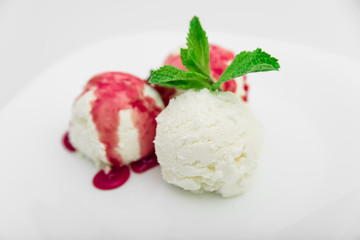 Three scoops of ice cream with strawberry syrup and mint on a white plate, white background, close-up
