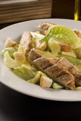 Caesar salad with croutons and grilled chicken on wooden table