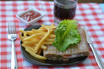 Big sandwich with fries covered with leaf lettuce