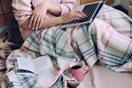Laptop on the girls knees nestled plaid and cup of coffee near the open book close up