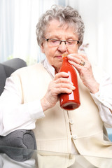 Babcine przetwory, przecier z czerwonych pomidorów. Starsza kobieta z butelką własnoręcznie przygotowanych przetworów z pomidorów.