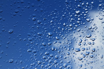 Rain drops on window with blue cloudy sky in background