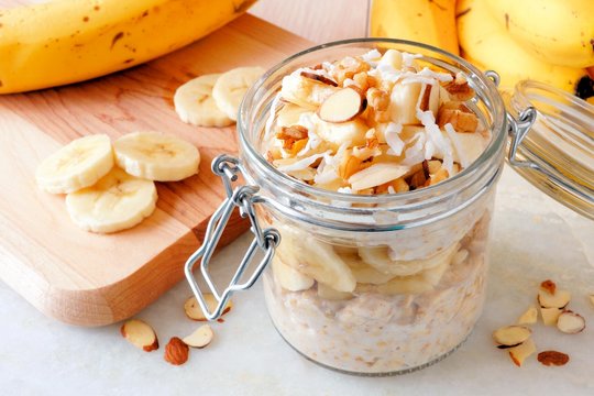 Overnight oats with bananas and nuts in snap lid glass jar on white marble