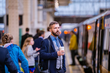 Hipster businessman with coffee cup at the train station