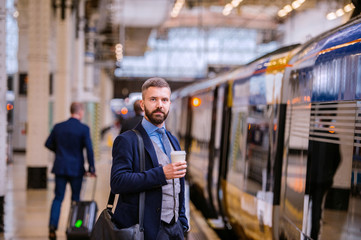 Hipster businessman with coffee cup at the train station