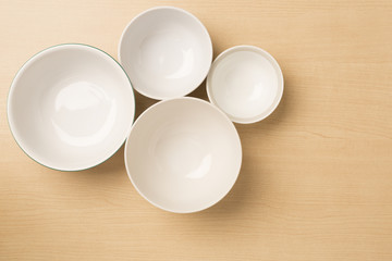 Four empty bowls on light wood background, top view