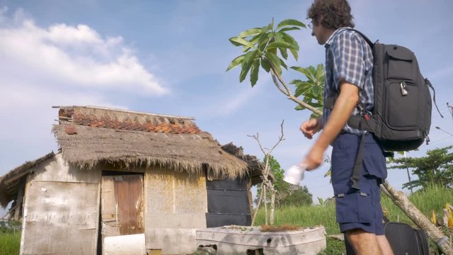 A tourist with baggage arrives to a run down hotel, villa, or guest house.