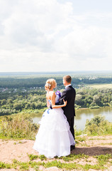 wedding couple hugging, the bride holding a bouquet of flowers,  groom embracing her outdoors