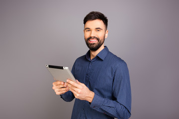 Handsome happy businessman holding tablet on gray background