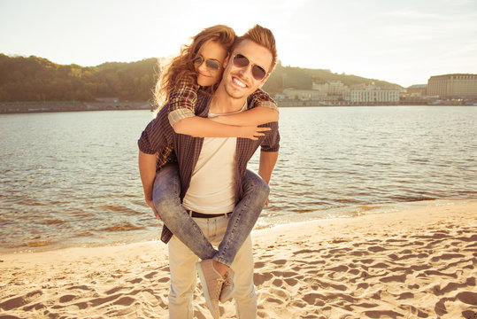 Happy young man piggybacking his pretty woman at the seaside