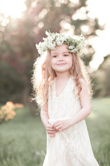 Smiling baby girl 3-4 year old wearing flower wreath outdoors. Little princess. Childhood.
