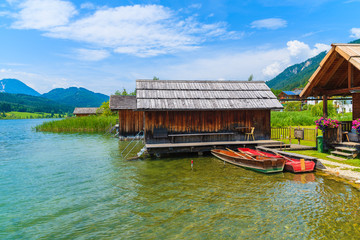 Fototapeta na wymiar Fishing boats and wooden houses on shore of Weissensee lake in summer landscape of Carinthia land, Austria