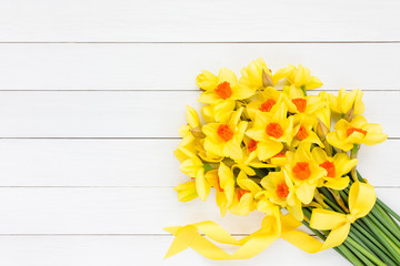 Bouquet of fresh spring narcissus decorated with ribbon on white wooden background. Top view, copy space 