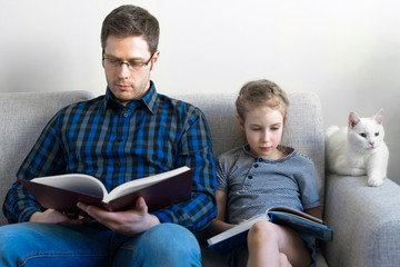 Father and his daughter reading books on sofa.
