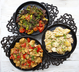 Three pig-iron frying pans with hot tasty food on a white wooden