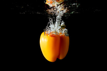 Yellow bulgarian pepper falls into the water isolated on the black background