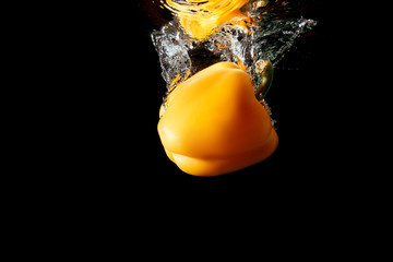 Yellow bulgarian pepper falls into the water isolated on the black background