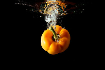Yellow bulgarian pepper falls into the water isolated on the black background