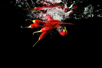 Several red peppers fallen into the water isolated on the black background