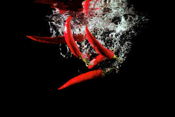 Several red peppers fallen into the water isolated on the black background