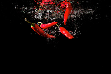 Several red peppers fallen into the water isolated on the black background