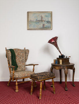 Retro ornate armchair, a 1911 old phonograph with three cylinder records on round coffee table and hanged painting on red carpet